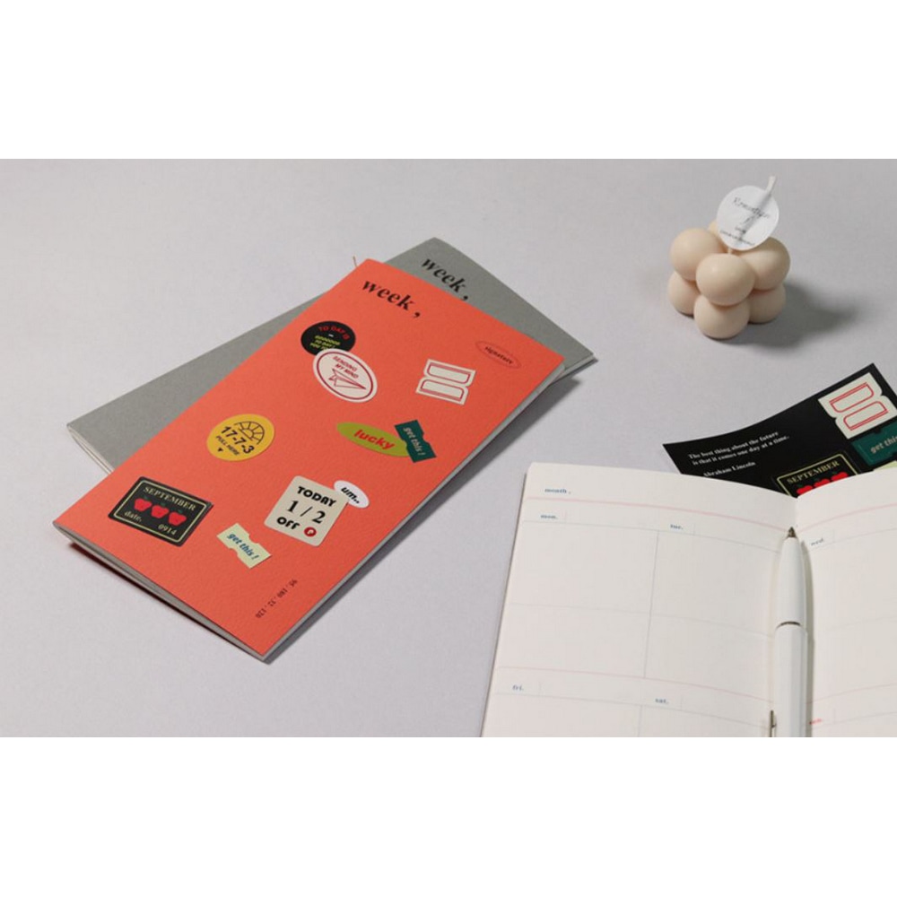 Signature Planner Weekly Tangerine mit Mingle Stickern beklebt auf einerm grauen Exemplar. Im Vordergrund ein offener Weekly planner ohne Eintrag.